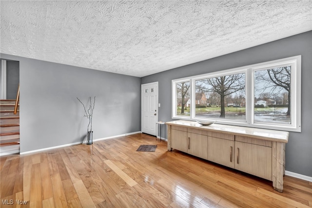 interior space featuring light wood-style floors, a textured ceiling, baseboards, and stairs