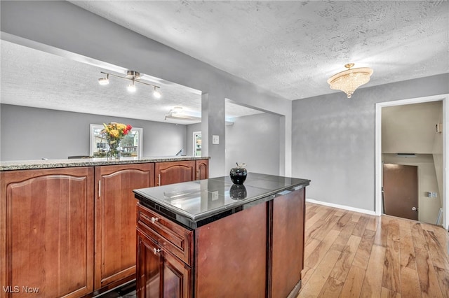 kitchen featuring baseboards, brown cabinets, a center island, a textured ceiling, and light wood-style floors