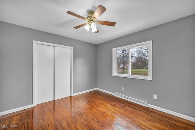 unfurnished bedroom featuring a baseboard radiator, a closet, a ceiling fan, wood finished floors, and baseboards