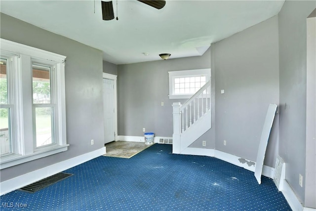 empty room with dark colored carpet, stairway, visible vents, and baseboards