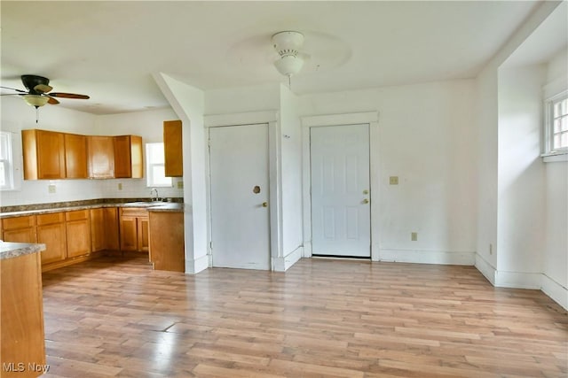 kitchen with a sink, a ceiling fan, baseboards, light wood-type flooring, and brown cabinetry