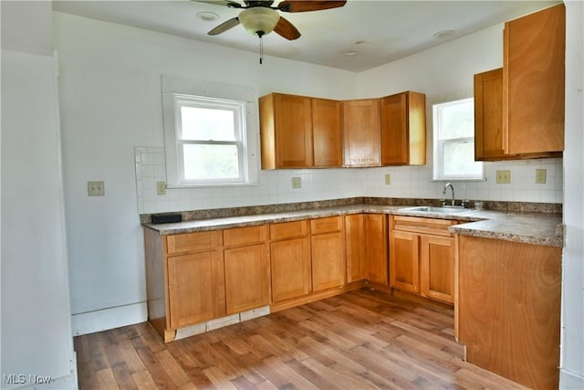 kitchen with backsplash, light wood-style flooring, brown cabinetry, a ceiling fan, and a sink