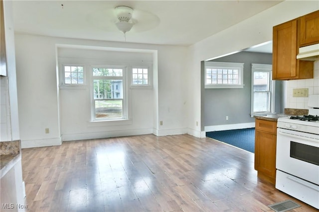 kitchen featuring white gas stove, light wood-type flooring, backsplash, and brown cabinets