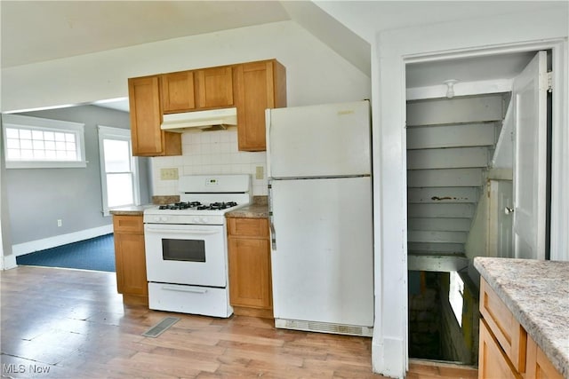 kitchen with under cabinet range hood, white appliances, light wood finished floors, light countertops, and tasteful backsplash