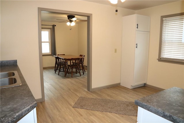 interior space featuring a ceiling fan, dark countertops, light wood-style flooring, and white cabinets