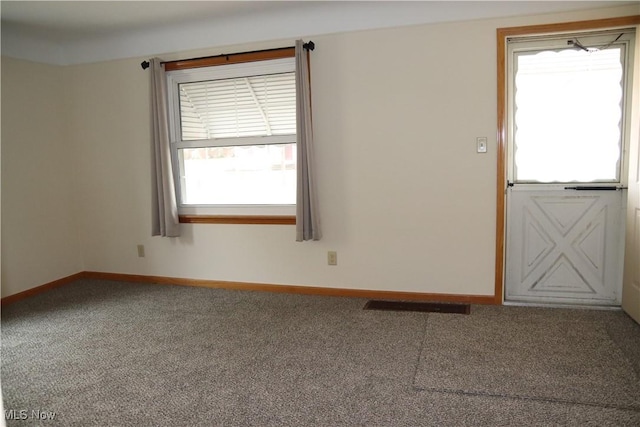 carpeted empty room featuring a wealth of natural light, visible vents, and baseboards