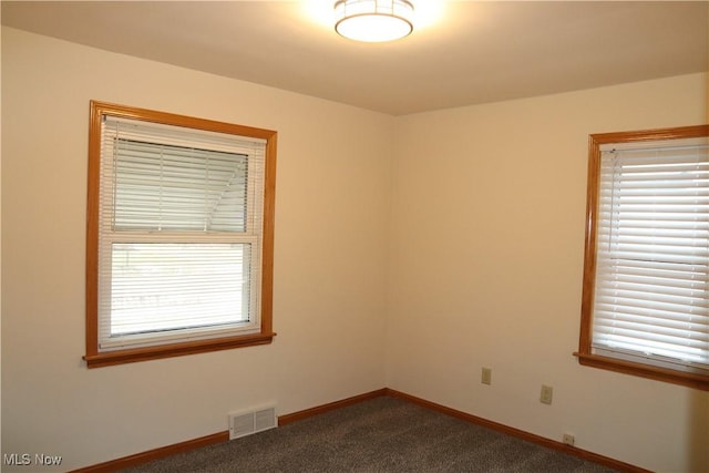 unfurnished room featuring dark colored carpet, a wealth of natural light, visible vents, and baseboards