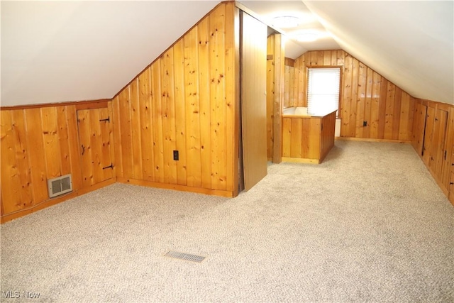 additional living space featuring light colored carpet, visible vents, vaulted ceiling, and wooden walls