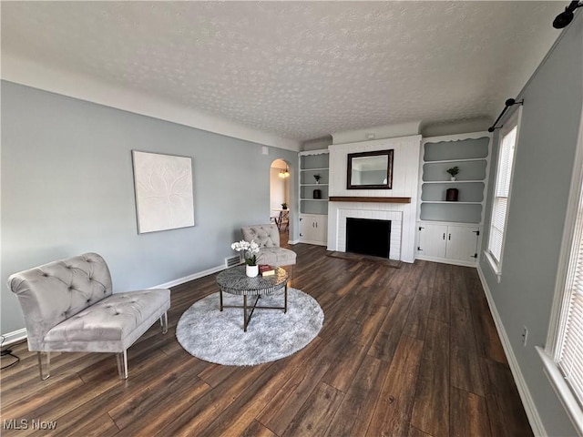 living room with a fireplace, arched walkways, dark wood-style flooring, and a textured ceiling