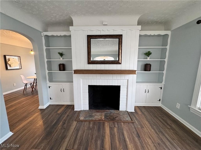 unfurnished living room with a textured ceiling, arched walkways, a fireplace, and dark wood-type flooring