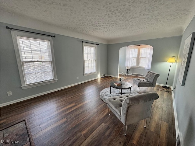 sitting room featuring baseboards, a textured ceiling, arched walkways, and dark wood-type flooring