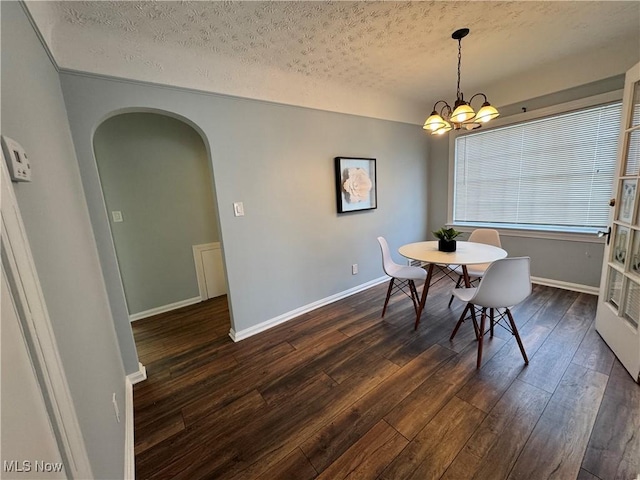 dining area with arched walkways, a textured ceiling, a notable chandelier, baseboards, and dark wood finished floors