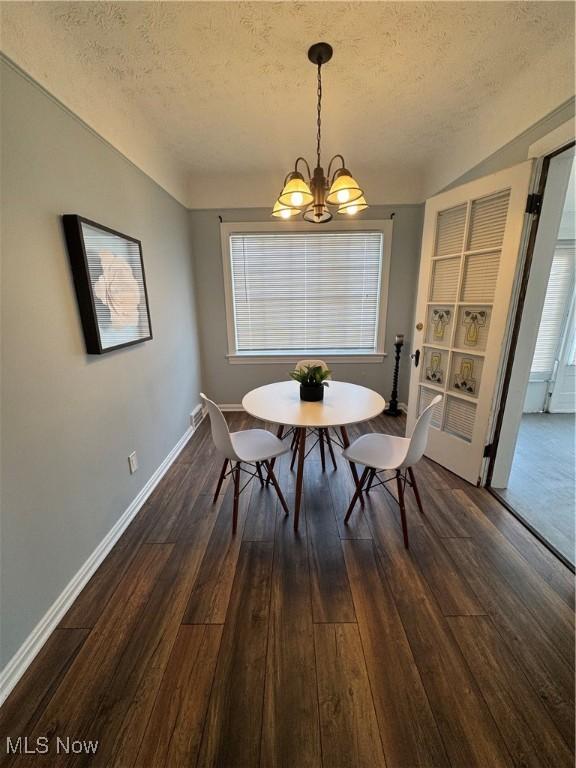 dining room with dark wood-type flooring, a textured ceiling, baseboards, and an inviting chandelier