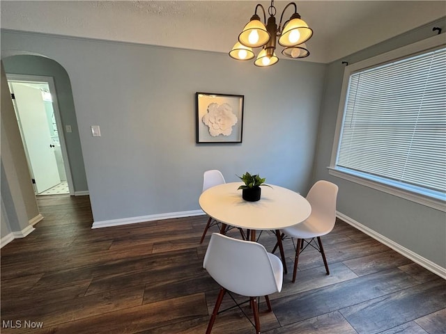 dining area with an inviting chandelier, baseboards, arched walkways, and dark wood-style flooring