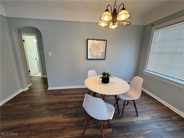 dining space with an inviting chandelier, baseboards, arched walkways, and dark wood-type flooring