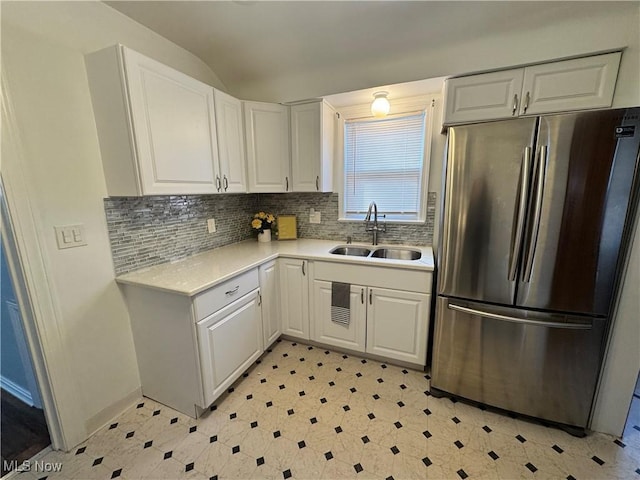 kitchen with light countertops, decorative backsplash, freestanding refrigerator, white cabinetry, and a sink