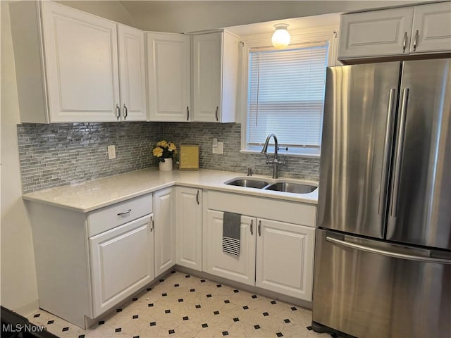 kitchen with a sink, white cabinets, light countertops, freestanding refrigerator, and decorative backsplash