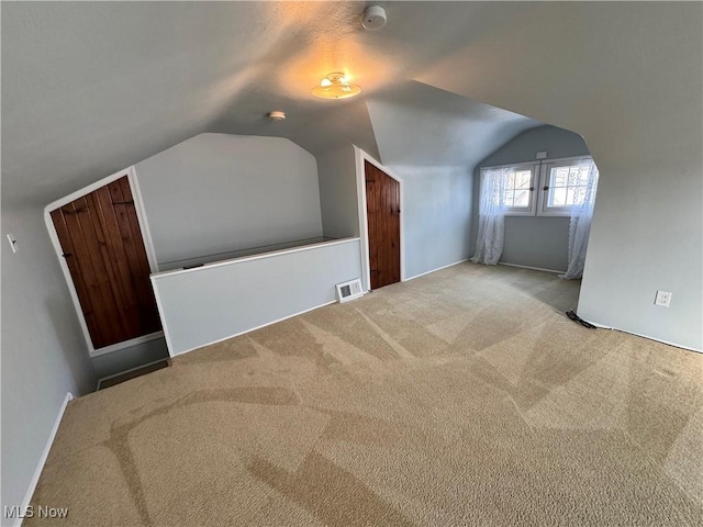 additional living space with light carpet, visible vents, and vaulted ceiling