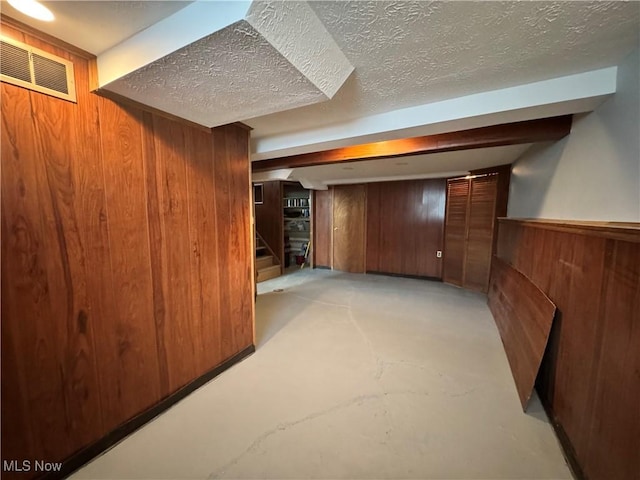 finished below grade area featuring visible vents, wainscoting, stairs, a textured ceiling, and wood walls