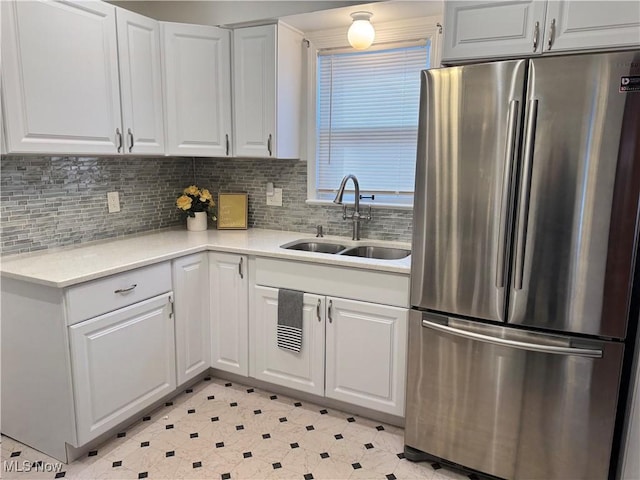 kitchen with light countertops, decorative backsplash, freestanding refrigerator, white cabinetry, and a sink