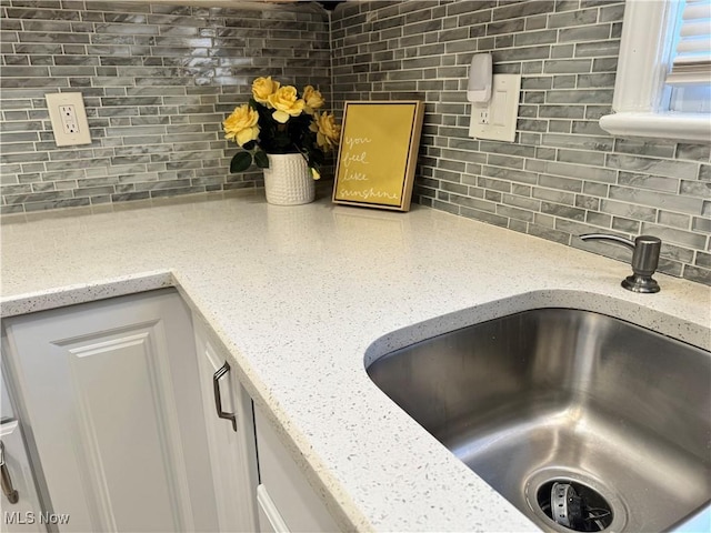 room details featuring a sink, backsplash, and light stone countertops