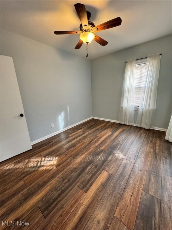 spare room with dark wood-type flooring, ceiling fan, and baseboards