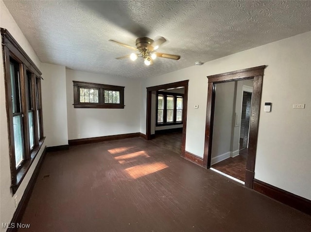 empty room featuring dark wood-style floors, ceiling fan, a textured ceiling, and baseboards