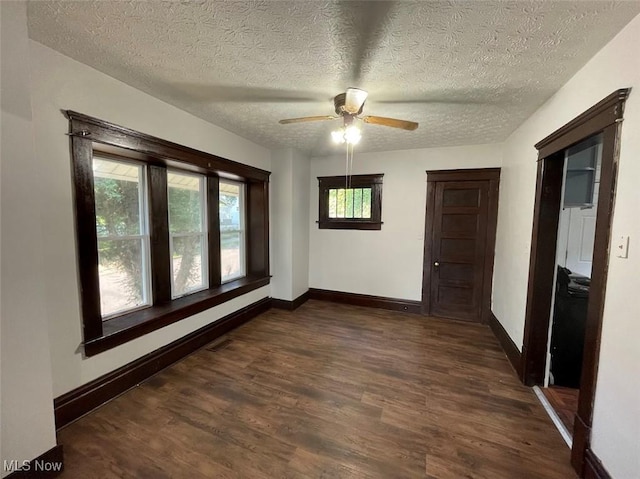 empty room with ceiling fan, a textured ceiling, baseboards, and dark wood-style flooring