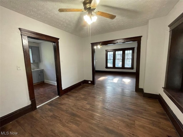 interior space with a ceiling fan, a textured ceiling, baseboards, and dark wood-type flooring