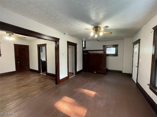 empty room with ceiling fan, dark wood-style flooring, a textured ceiling, and baseboards