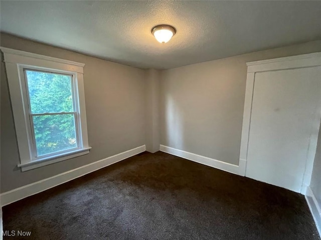 empty room with a textured ceiling, dark colored carpet, and baseboards