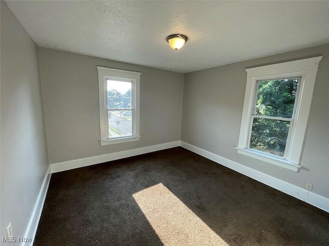 empty room featuring a textured ceiling, dark colored carpet, and baseboards