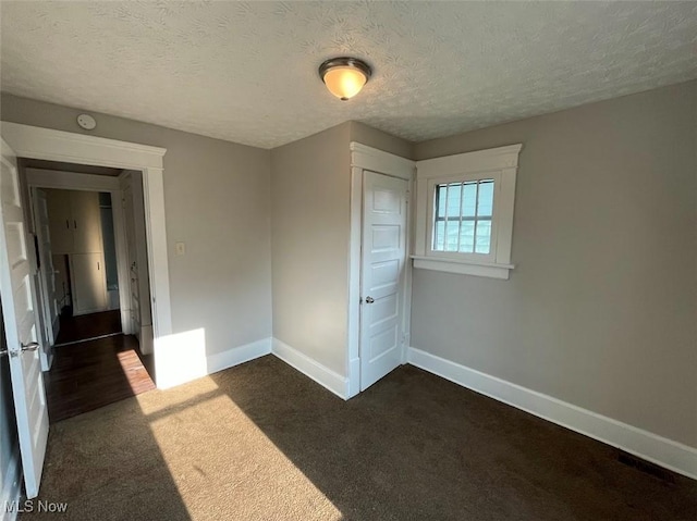 unfurnished bedroom featuring dark colored carpet, a textured ceiling, and baseboards