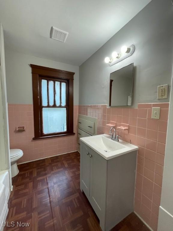 bathroom featuring toilet, visible vents, tile walls, and wainscoting