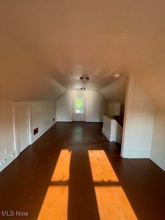 bonus room featuring dark wood-style floors, visible vents, vaulted ceiling, and baseboards