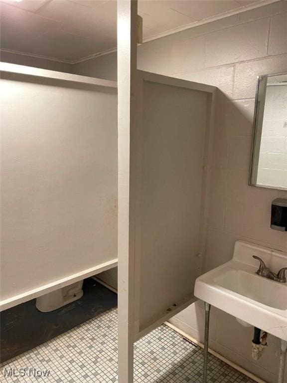 bathroom featuring concrete block wall, a sink, crown molding, and tile patterned floors