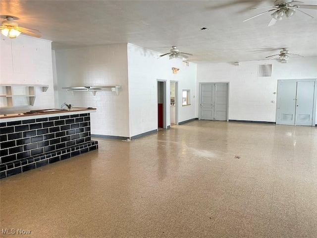 interior space with baseboards, a ceiling fan, and concrete block wall