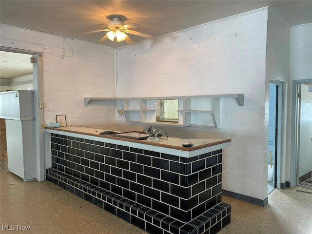 bar featuring a ceiling fan, freestanding refrigerator, and concrete block wall