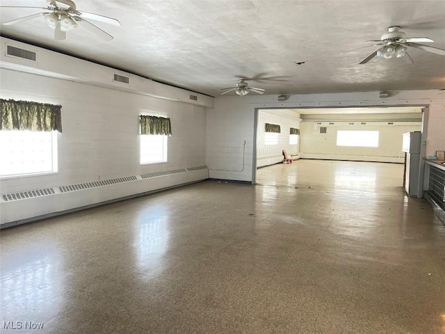 interior space with a ceiling fan, a baseboard radiator, visible vents, and plenty of natural light