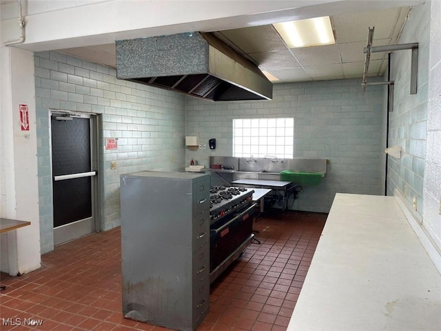 kitchen with light countertops, double oven range, wall chimney range hood, and dark tile patterned flooring