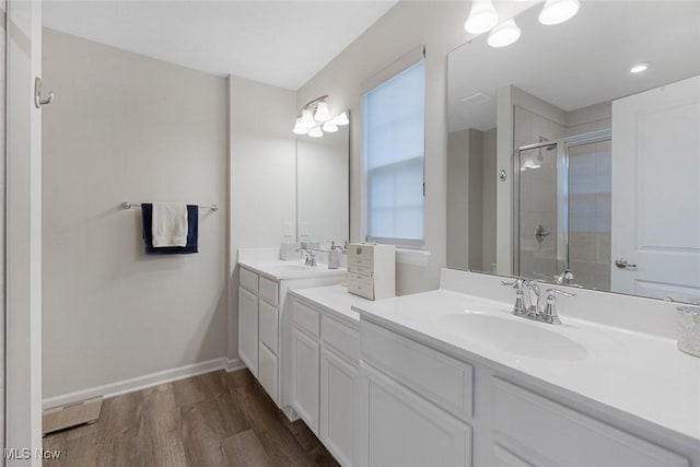 bathroom with double vanity, a sink, a shower stall, wood finished floors, and baseboards