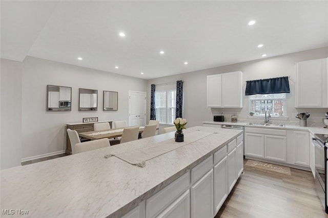 kitchen with a sink, white cabinetry, light wood-style floors, light countertops, and plenty of natural light