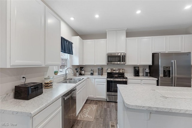 kitchen featuring recessed lighting, appliances with stainless steel finishes, white cabinets, a sink, and wood finished floors