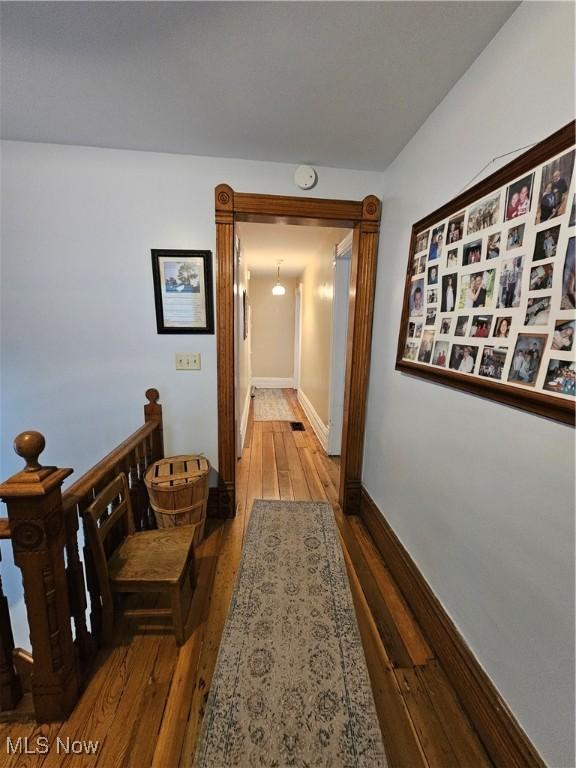 hallway featuring wood finished floors, an upstairs landing, and baseboards