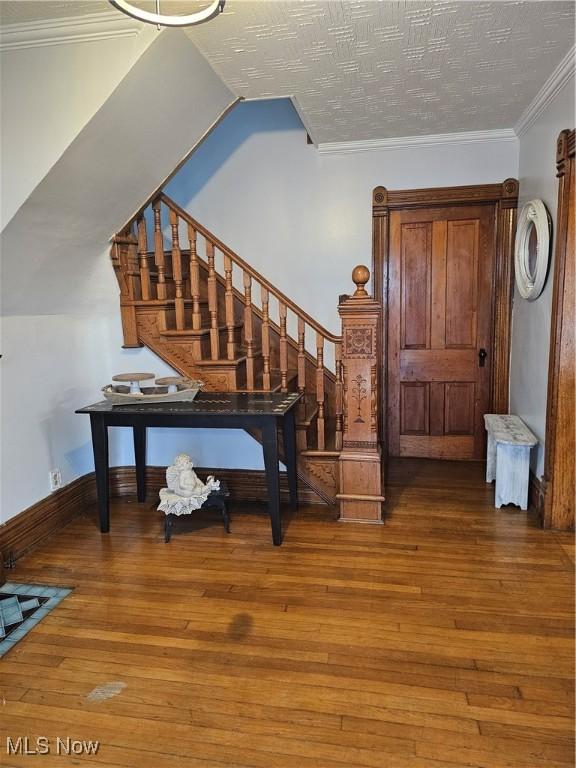 interior space featuring crown molding, a textured ceiling, wood finished floors, baseboards, and stairs