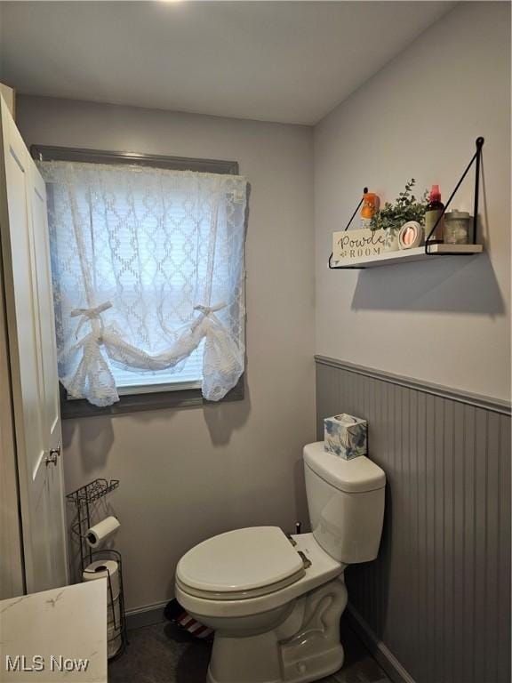 half bath featuring a wainscoted wall and toilet