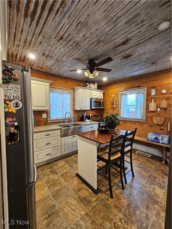 kitchen featuring stainless steel appliances, wood ceiling, a sink, wood walls, and butcher block countertops