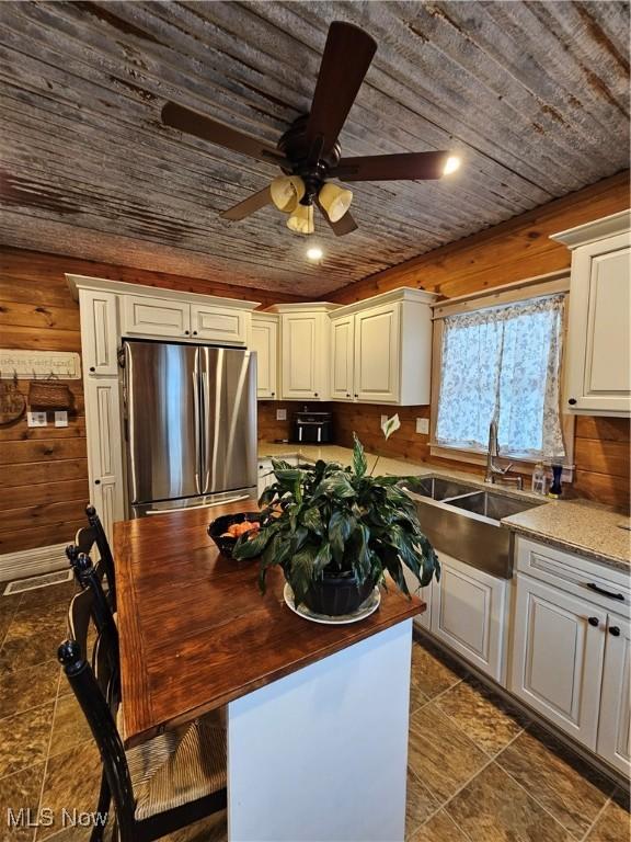 kitchen featuring freestanding refrigerator, wood ceiling, white cabinetry, a sink, and wooden walls