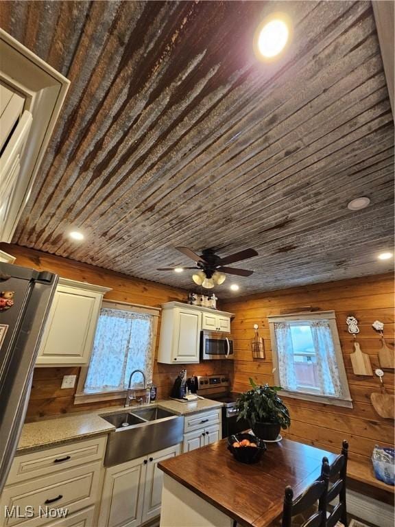 kitchen with wooden ceiling, wooden walls, stainless steel appliances, a sink, and a ceiling fan