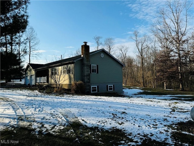 view of snowy exterior with a garage and a chimney